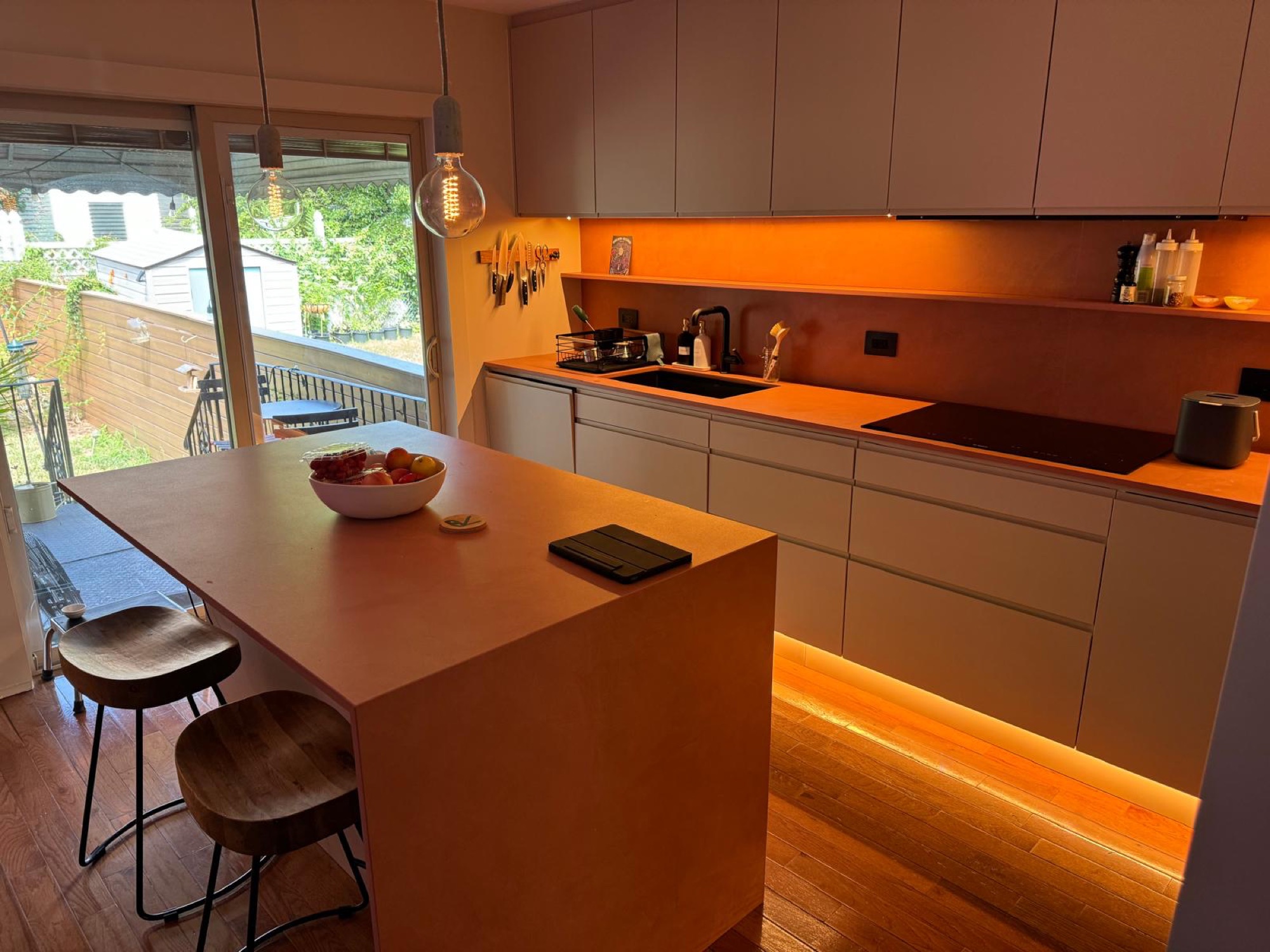 Modern handleless kitchen with terracotta-toned waterfall island and garden doors open to the backyard