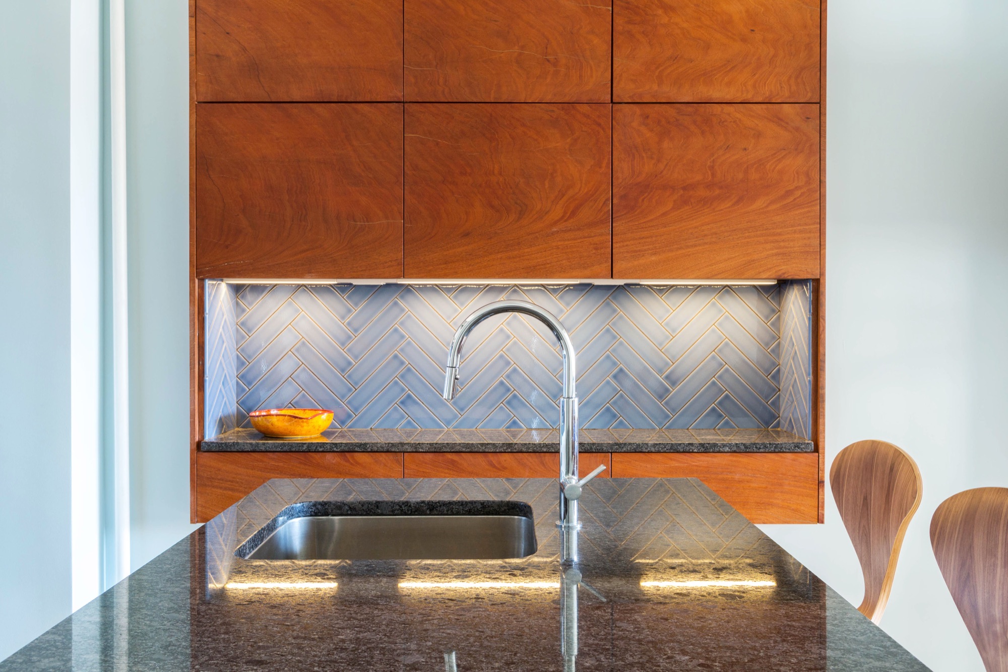 Mahogany upper cabinets and blue herringbone glass tile backsplash over a black stone counter